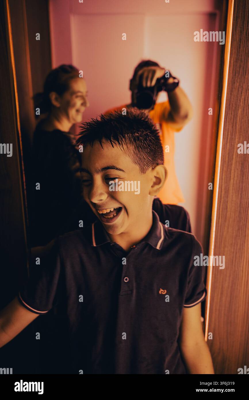 Enfant riant avec sa famille réfléchie dans un miroir sous un éclairage intérieur chaud Banque D'Images