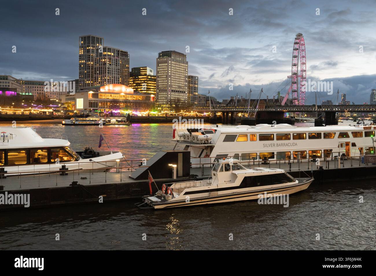 Les bateaux fluviaux accostent au quai de Woods sur la Tamise au crépuscule, avec le London Eye et la Royal Festival Hall illuminés sur la rive sud. Banque D'Images