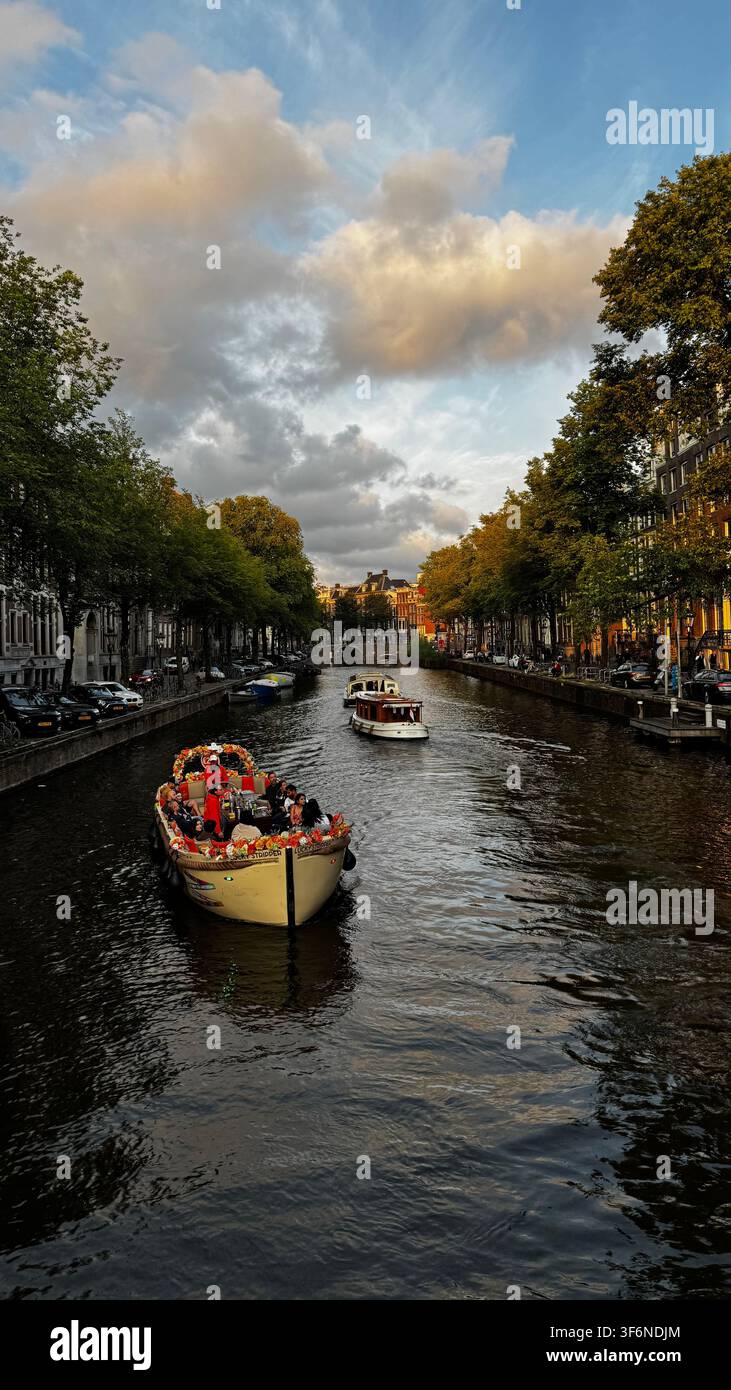 Croisière sur les canaux d'Amsterdam à l'heure dorée – Bateaux, maisons de canal et voie d'eau bordée d'arbres, Pays-Bas - Image de stock capturée avec un smartphone
