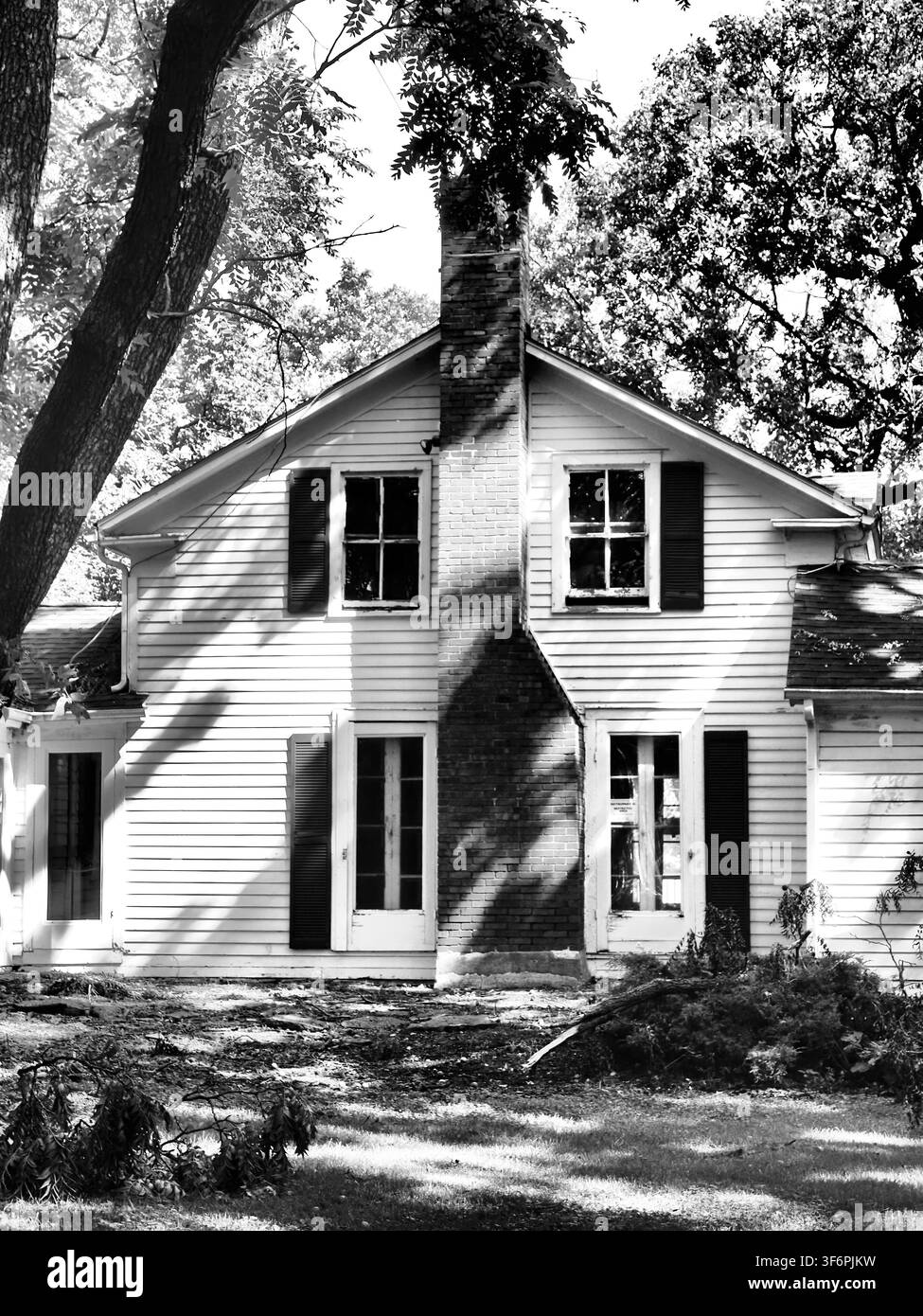 Photo noir et blanc de l'extérieur d'une vieille maison historique en bois blanc avec une cheminée centrale en brique et des volets vintage Banque D'Images
