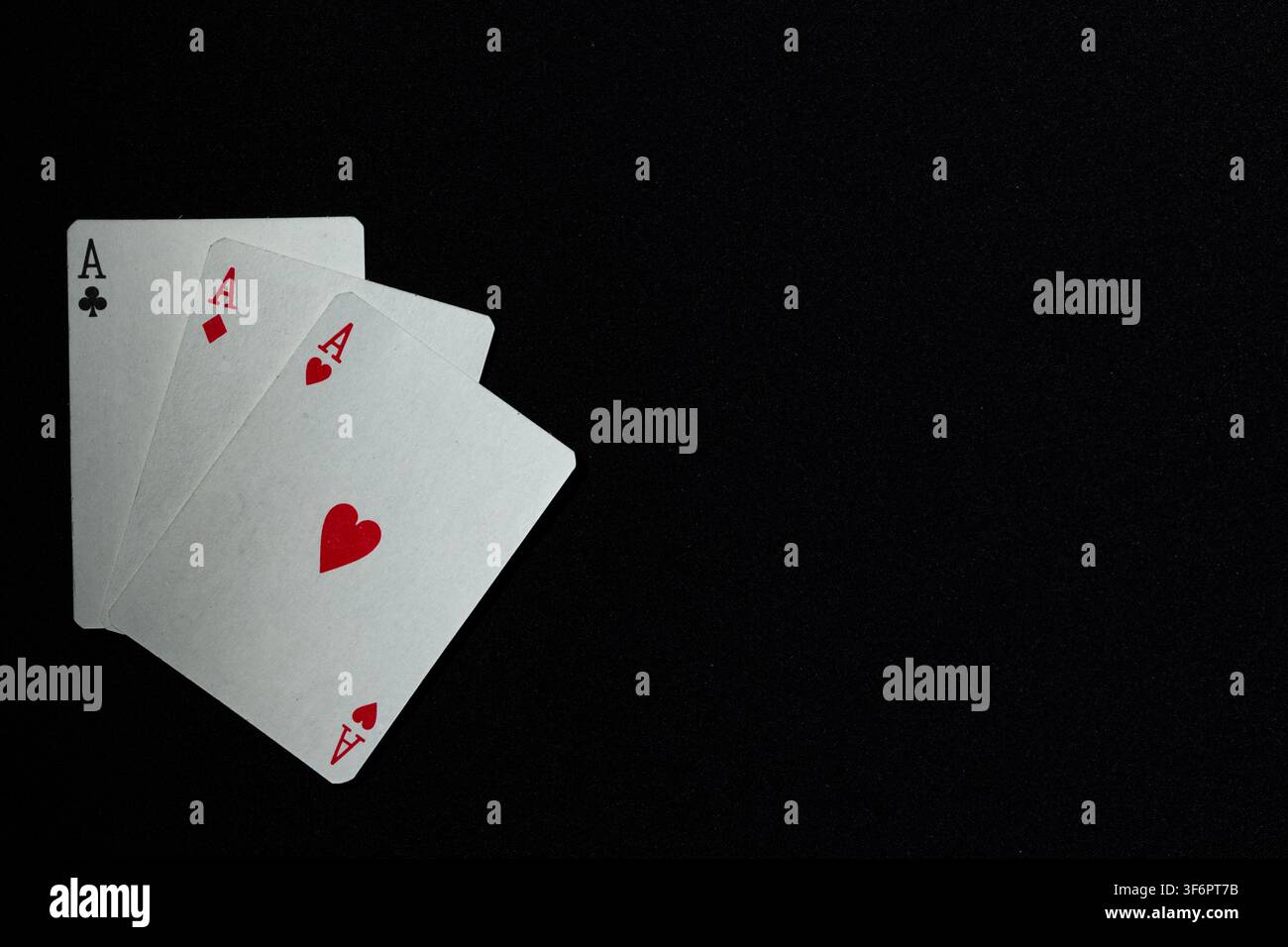 Trois cartes à jouer, les as de trèfle, de carreau et de cœur sur un fond en tissu sombre moucheté, suggérant le succès, l’habileté et la chance. Banque D'Images