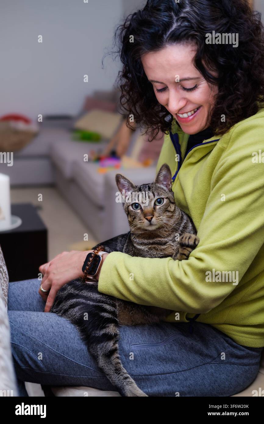 Femme souriante, caressant un chat tigré sur ses genoux, partageant des moments d'amitié Banque D'Images