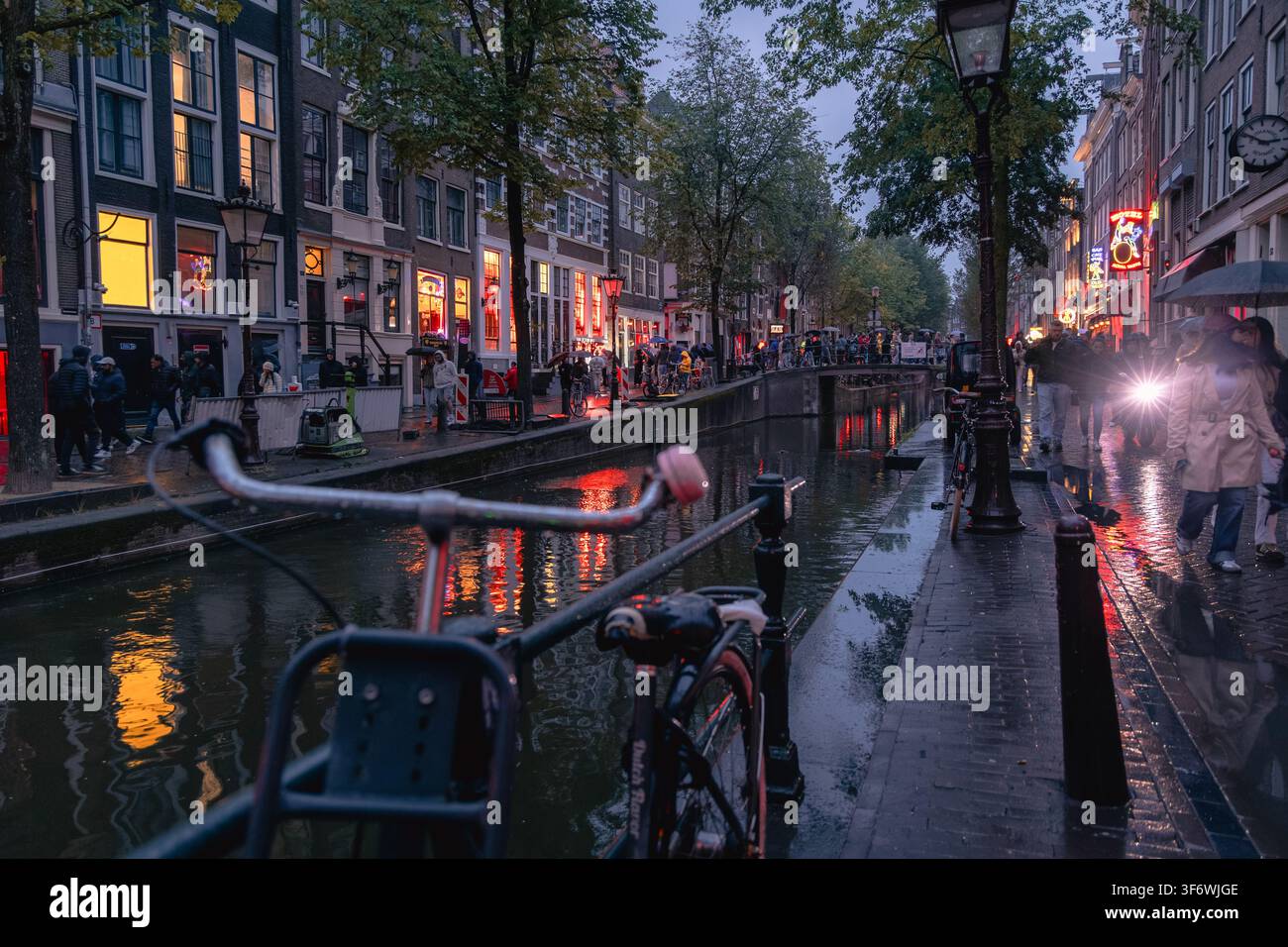 Touristes et habitants explorant le quartier De Wallen le long du canal Oudezijds Voorburgwal, illuminé par des néons rouges se reflétant sur le pavé mouillé Banque D'Images