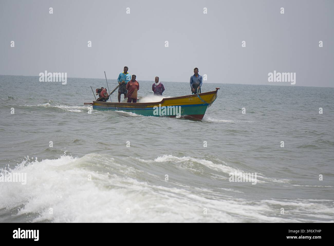 Des pêcheurs indiens debout à bord d'un bateau à moteur coloré naviguant le long des eaux côtières. Banque D'Images