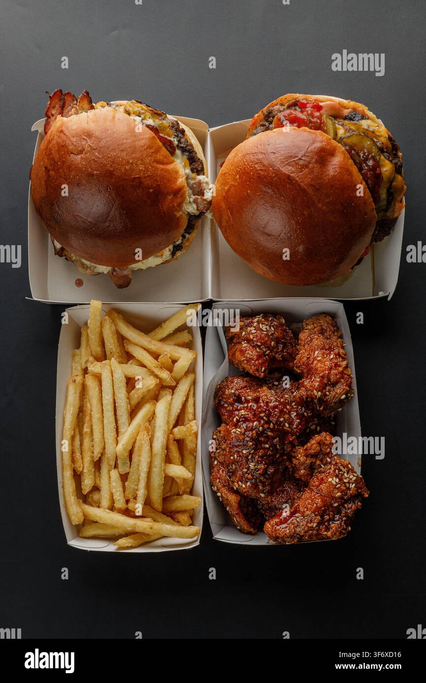Vue de dessus de hamburgers, poulet et frites sur fond noir Banque D'Images
