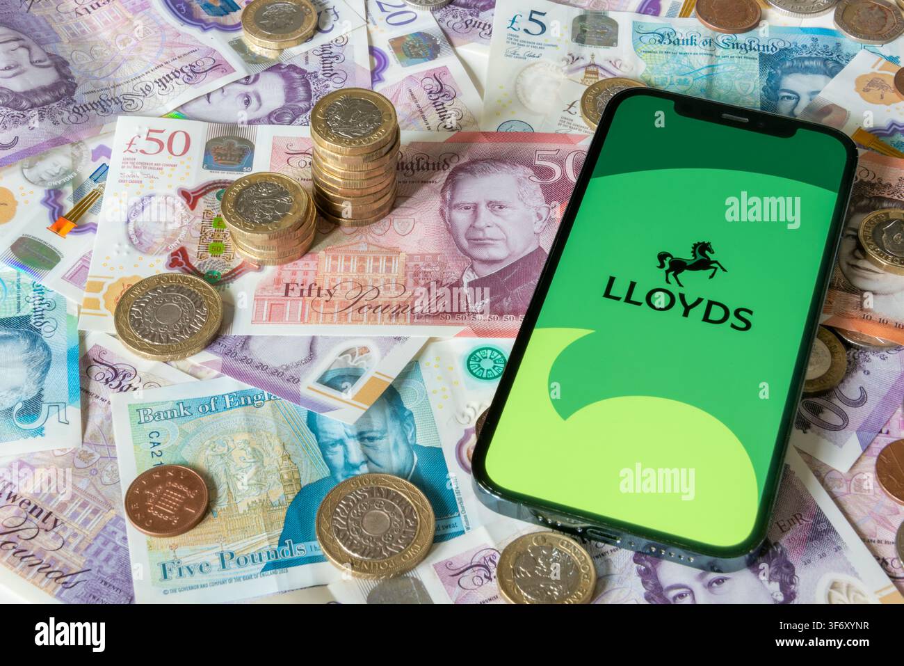 Application bancaire Lloyds Bank avec des billets et pièces en livres sterling en arrière-plan Banque D'Images