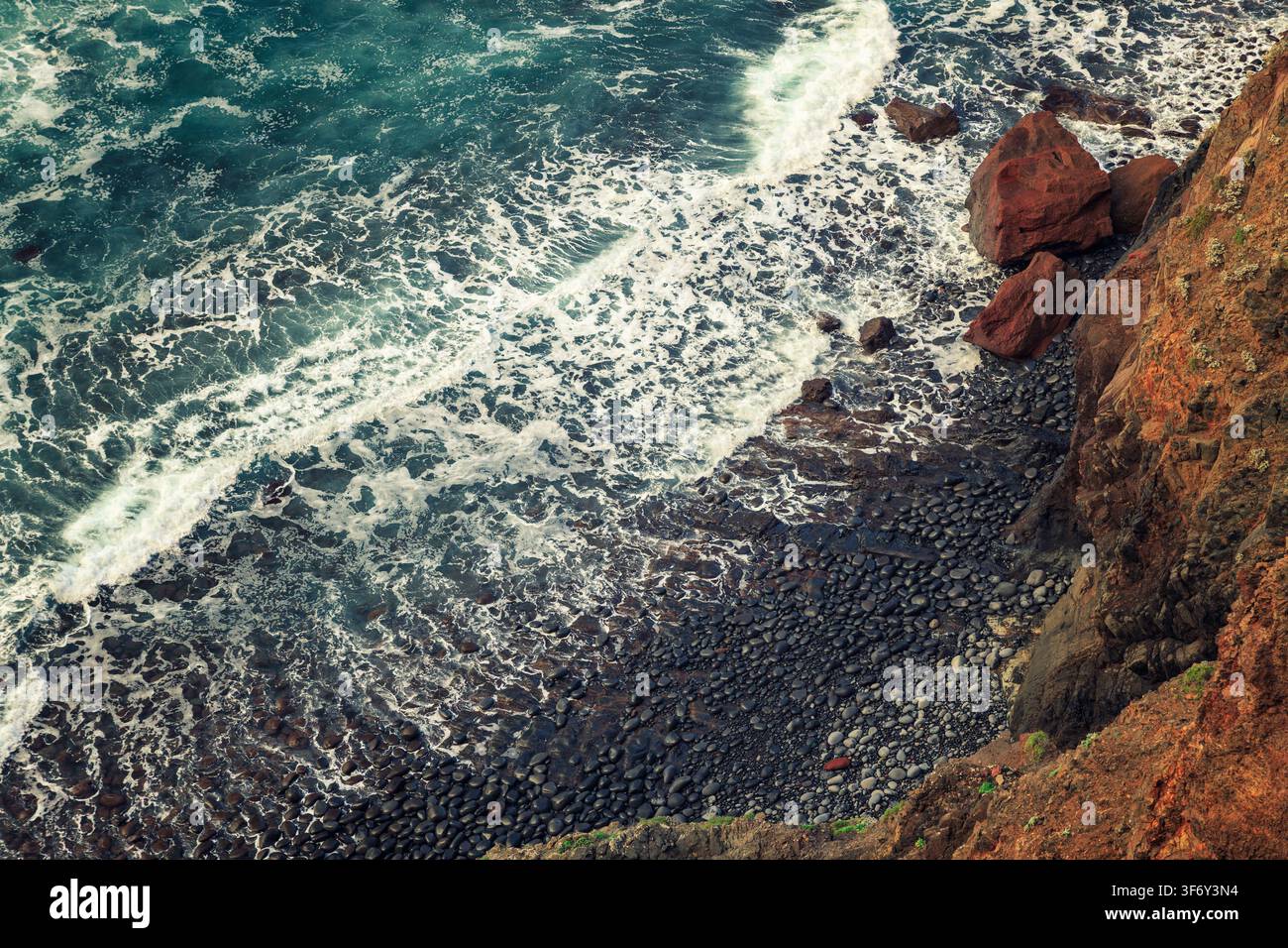 Caniçal, Portugal - 01.12.2025 : Mousse de mer blanche dramatique déferlant sur des pierres volcaniques sombres au pied de falaises côtières brunâtres abruptes Banque D'Images