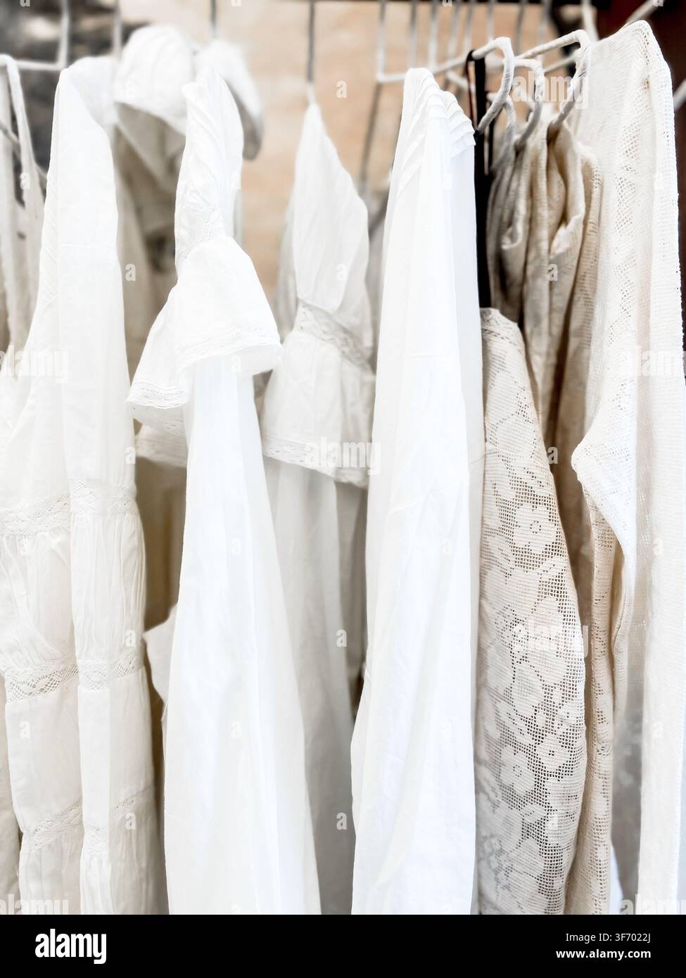 Collection de vêtements élégants blancs et beiges avec des détails en dentelle délicate suspendus sur un portant à vêtements Banque D'Images