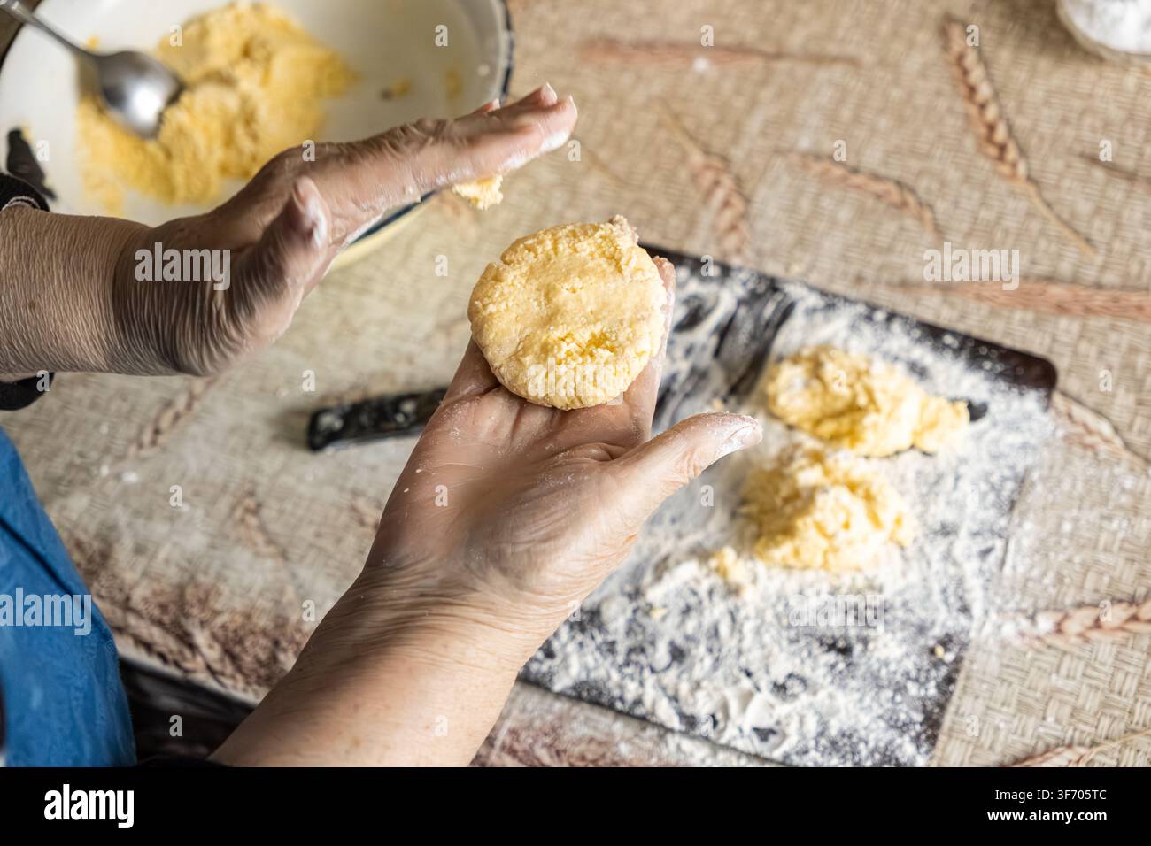 Une personne forme de petites galettes de pâte à partir de fromage frais pour les faire frire à la poêle, mettant l'accent sur le processus manuel de fabrication des syrniki dans une cuisine chaleureuse à la maison Banque D'Images