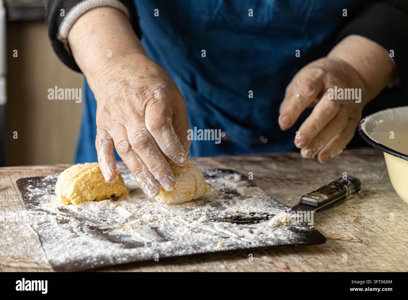 Vue rapprochée d'une femme âgée préparant la pâte pour des syrniki traditionnels sur une table en bois, mettant l'accent sur la préparation tactile de la nourriture faite maison et le temps Banque D'Images
