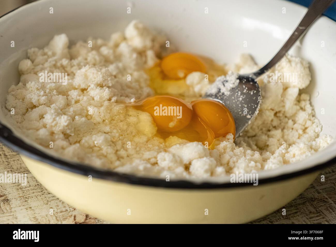 Close-up d'œufs frais cassés dans du fromage à pâte molle pour la préparation traditionnelle des syrniki, évoquant un sentiment de cuisine maison saine pendant une expérience culinaire Banque D'Images
