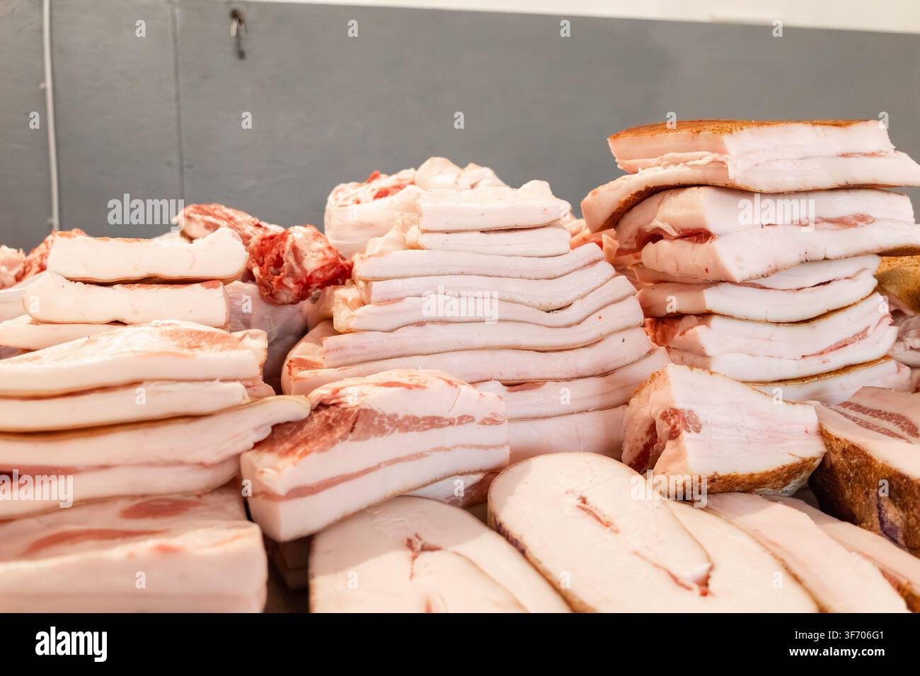 Des rangées de lard de porc cru tranché et de bacon salé sont empilées sur une table dans une boucherie, mettant en valeur des ingrédients artisanaux de haute qualité essentiels pour la tradition Banque D'Images