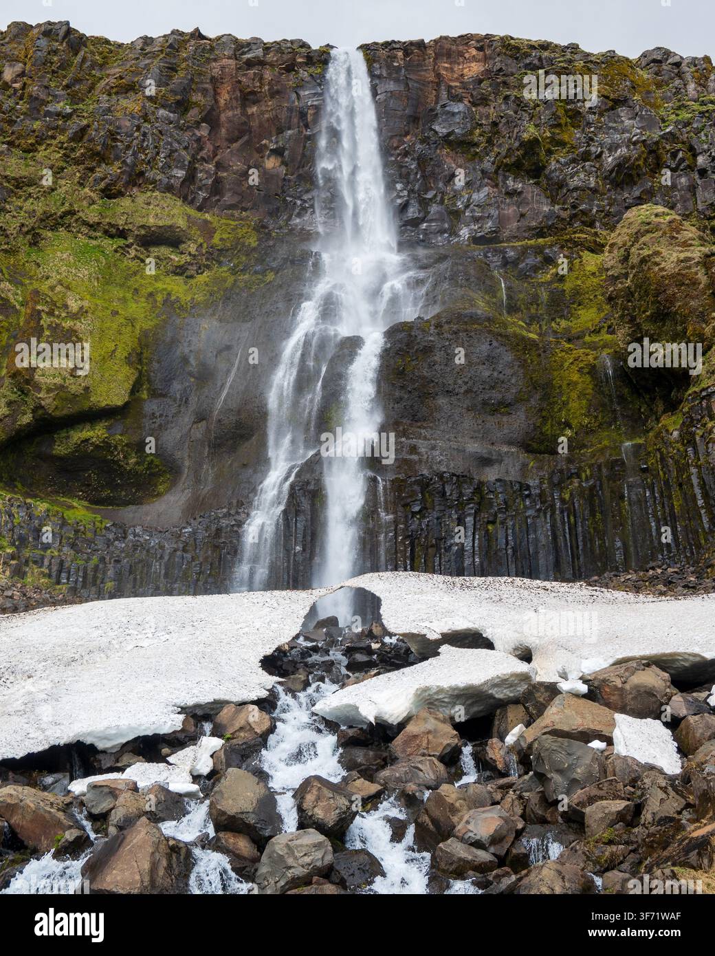 La cascade de Bjarnarfoss dévale des colonnes de basalte sombres et une plaque de neige, péninsule de Snæfellsnes, Islande. Banque D'Images