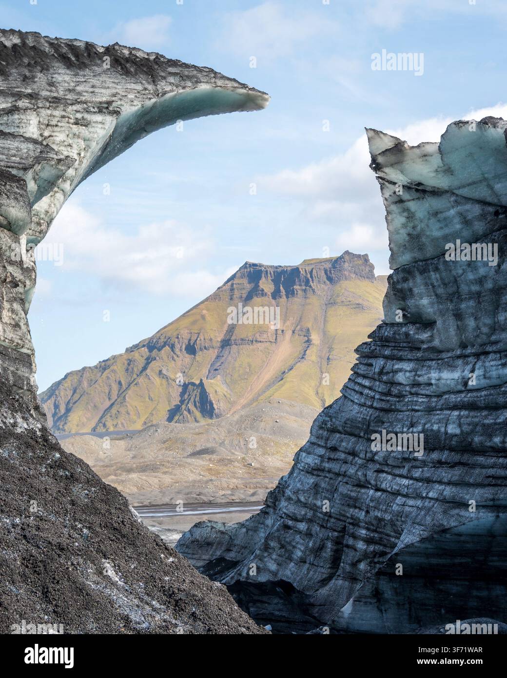 Deux cornes incurvées de glace glaciaire encadrent une vue sur les montagnes lointaines des hautes terres à travers une plaine volcanique noire, Islande. Banque D'Images