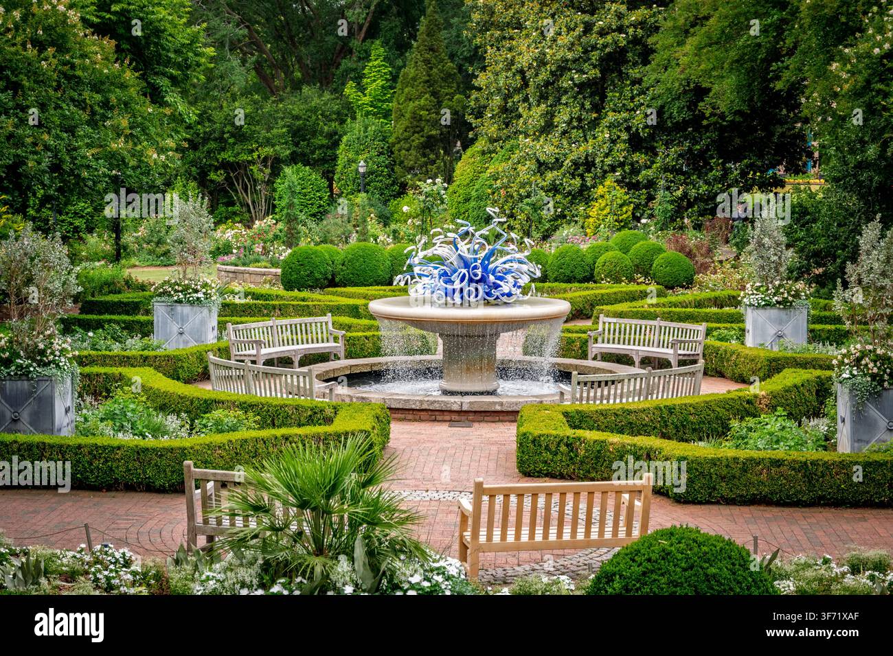 Atlanta, Géorgie – Mai 2026 : Une sculpture en verre bleu cobalt couronne une fontaine en pierre dans un jardin formel de buis au Jardin botanique d'Atlanta. Banque D'Images