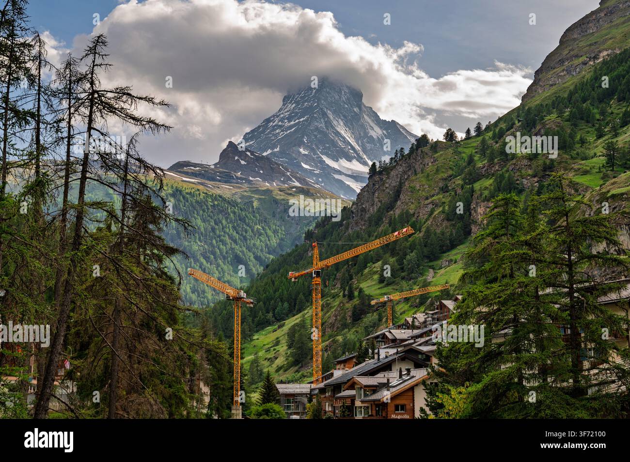 Zermatt, Suisse - juin 2026 : le Matterhorn émerge des nuages au-dessus de chalets en bois, d’un bâtiment marqué Magnolia et de grues de construction. Banque D'Images