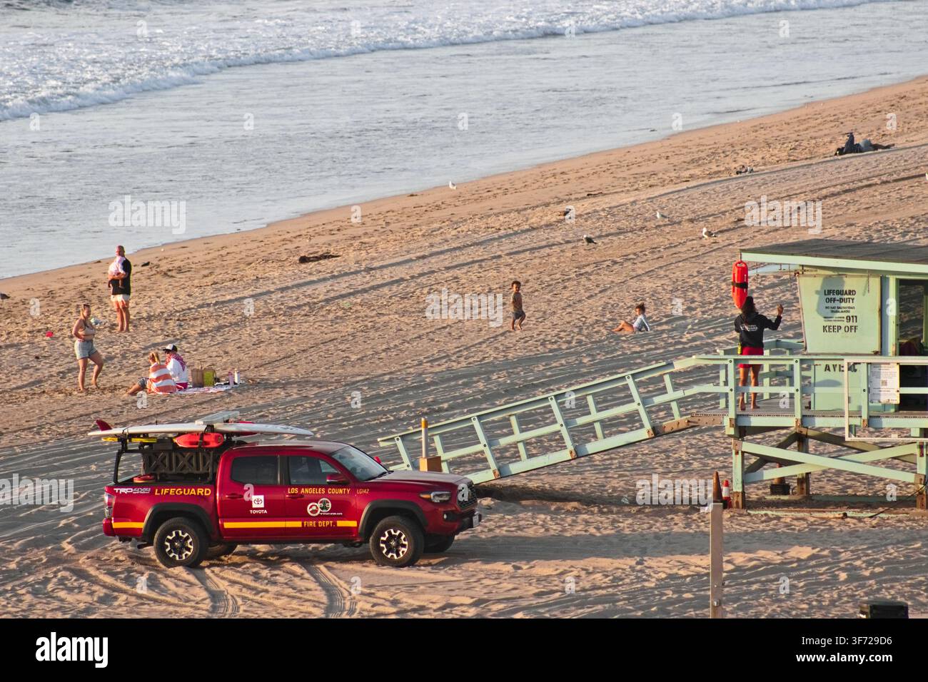 Une tour de sauvetage et un camion de sauvetage du comté de Los Angeles se trouvent sur la plage de sable tandis que des visiteurs marchent le long du rivage près de l'océan Pacifique. Banque D'Images