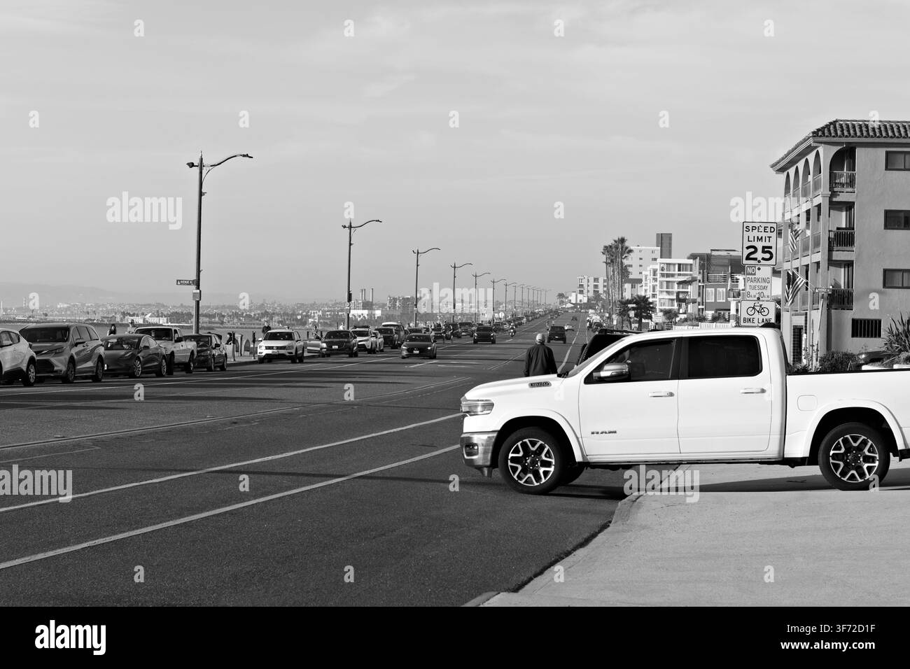 Un pick-up blanc s'arrête au coin d'une rue en ville. Les voies du tramway traversent la route. Des voitures garées bordent le trottoir. Un bâtiment aux tuiles rouges s'élève au loin. Banque D'Images