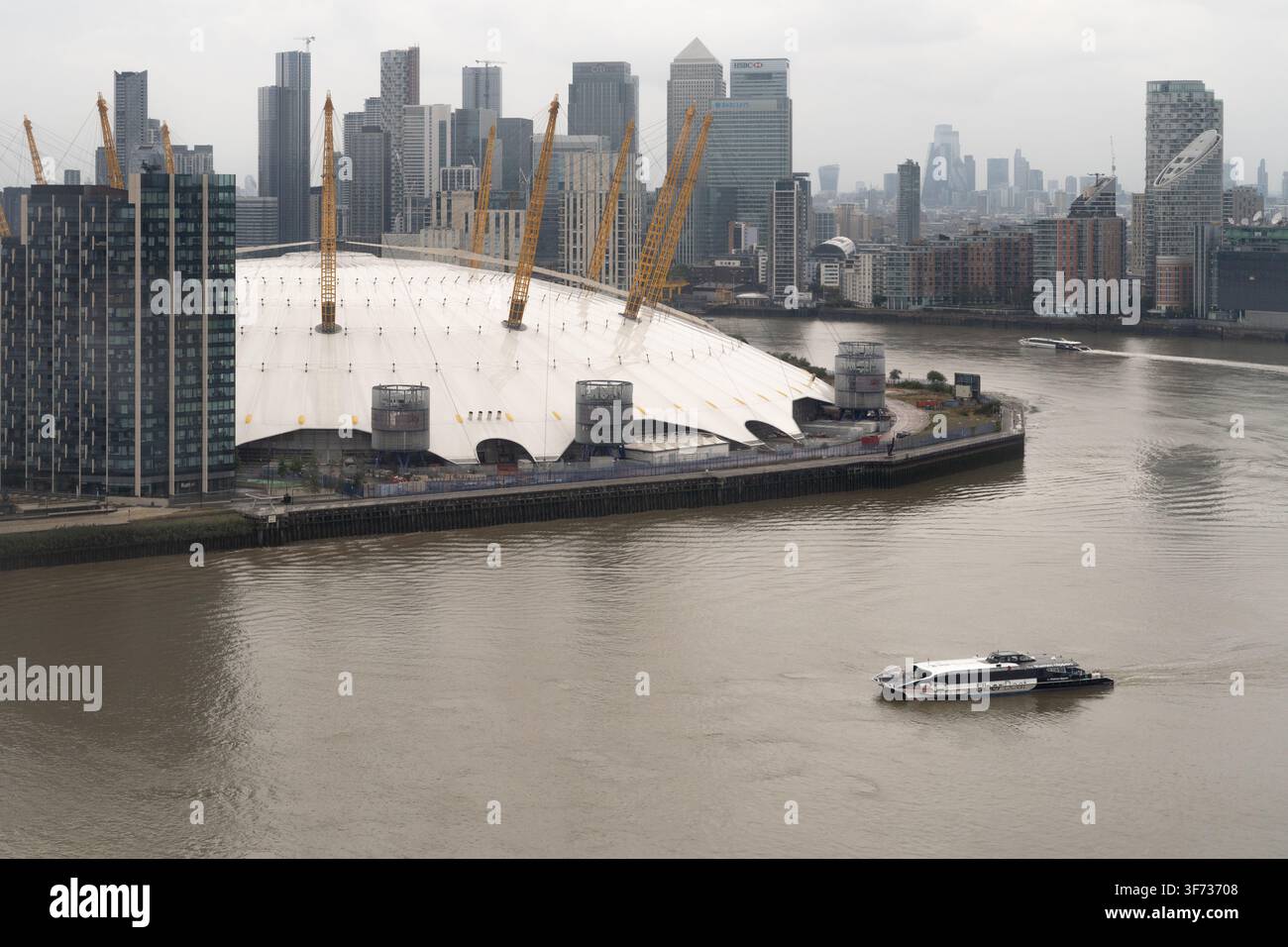 Un Uber Boat parcourt la Tamise devant l'O2 Arena à North Greenwich, offrant un transport essentiel contre le ciel urbain de Londres. Banque D'Images