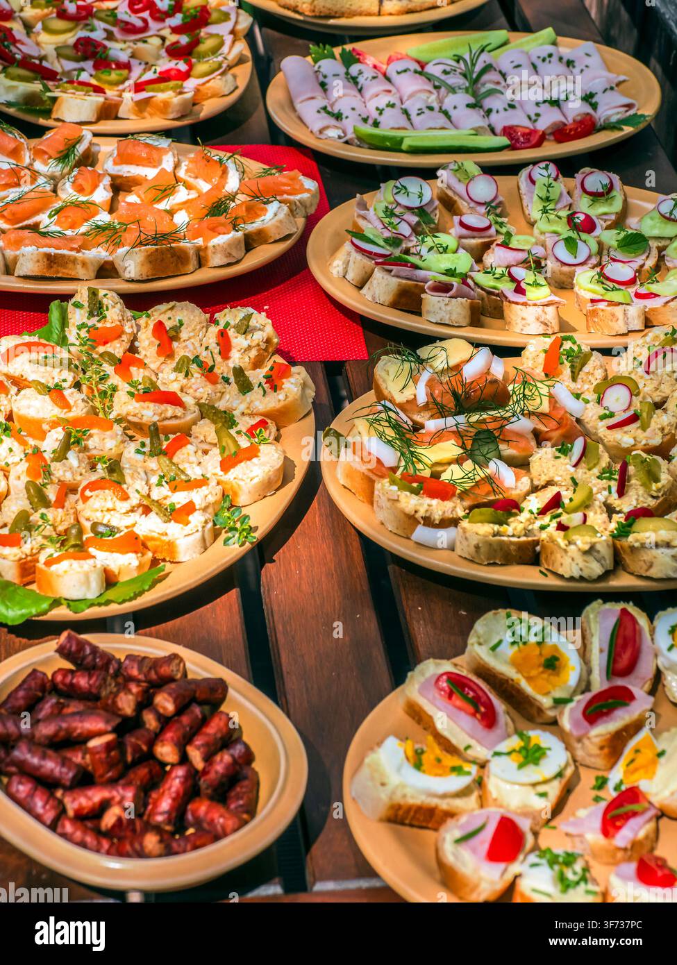 Canapés colorés variés et finger foods disposés sur des plateaux pour une fête ou un buffet : saumon fumé, bouchées d'œufs, roulés au jambon, cornichons et herbes créant Banque D'Images