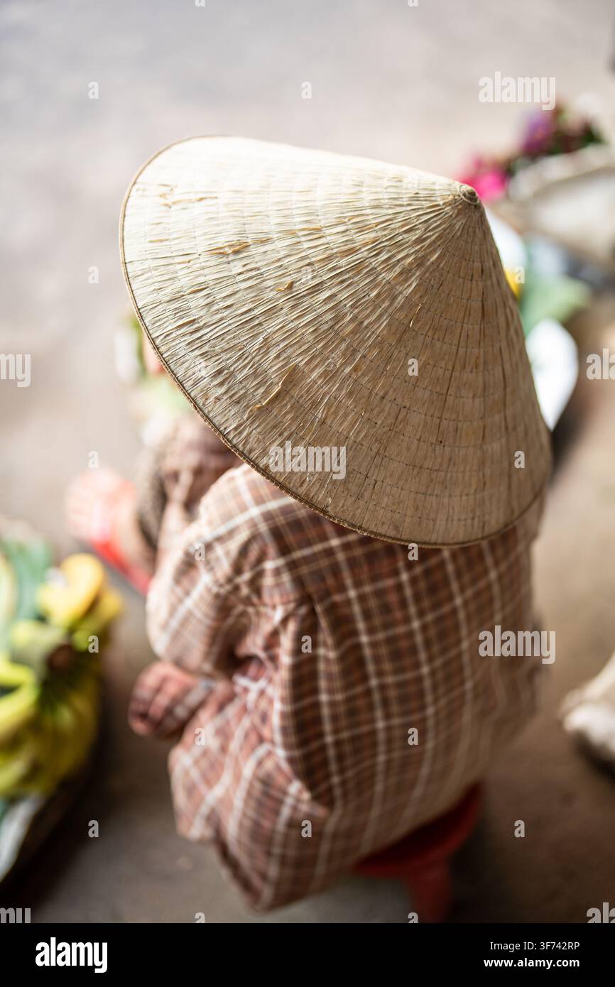 Vendeur de marché de rue méconnaissable portant un chapeau conique traditionnel, assis en attendant les clients. Banque D'Images
