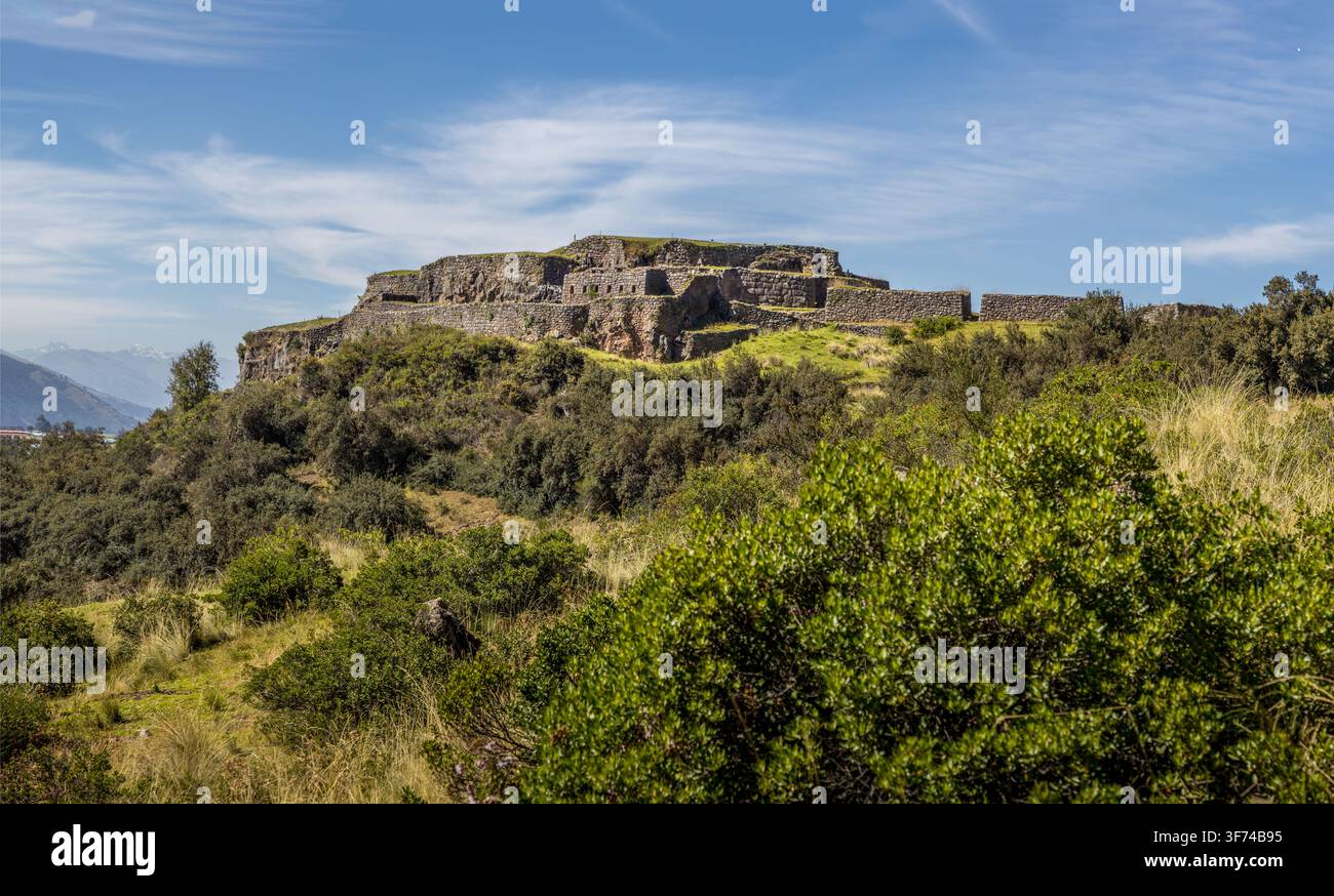 Ancienne forteresse inca de Puka Pukara s'élevant au-dessus des murs de pierre en terrasses et de la végétation luxuriante des Andes avec un paysage montagneux au loin sous un ciel bleu clair Banque D'Images