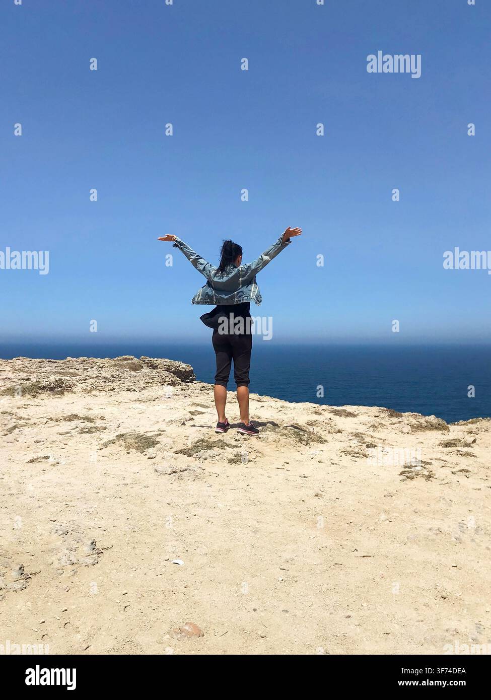 Femme debout sur une falaise les bras grands ouverts contemplant l'océan Atlantique au Portugal, concept de liberté et de réussite avec espace de copie. Banque D'Images