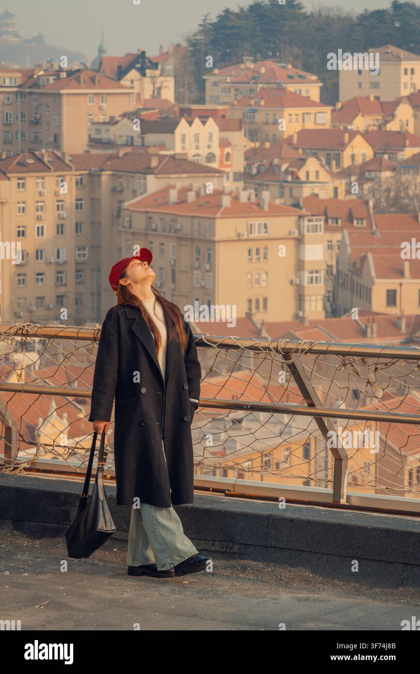 Femme les yeux fermés profitant de la brise du coucher de soleil sur un toit, Qingdao, Chine Banque D'Images