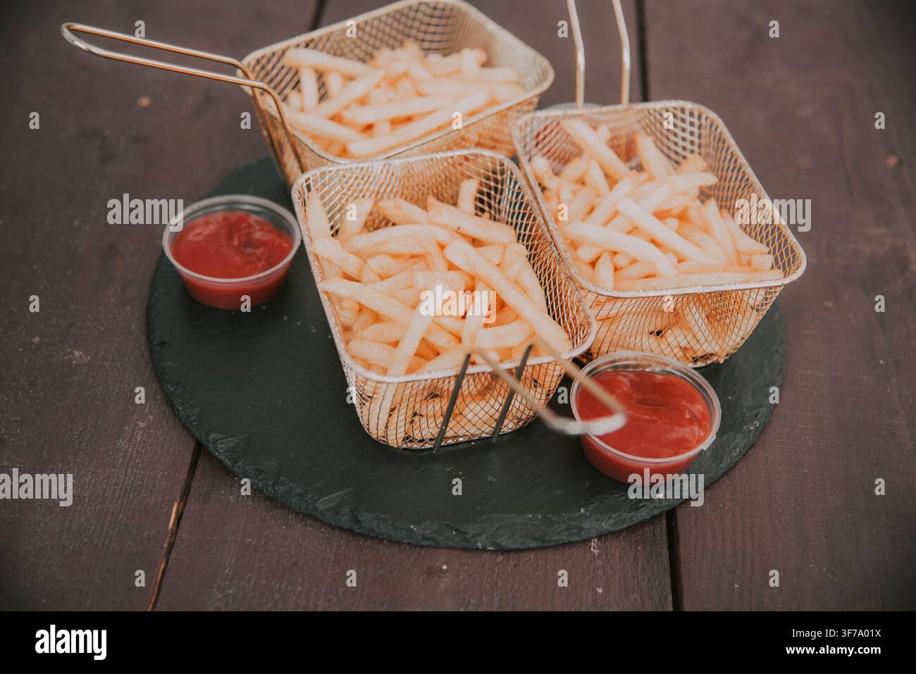Belle portion de frites avec ketchup. Frites dans un panier de service avec sauce sur un plateau de pierre. Banque D'Images