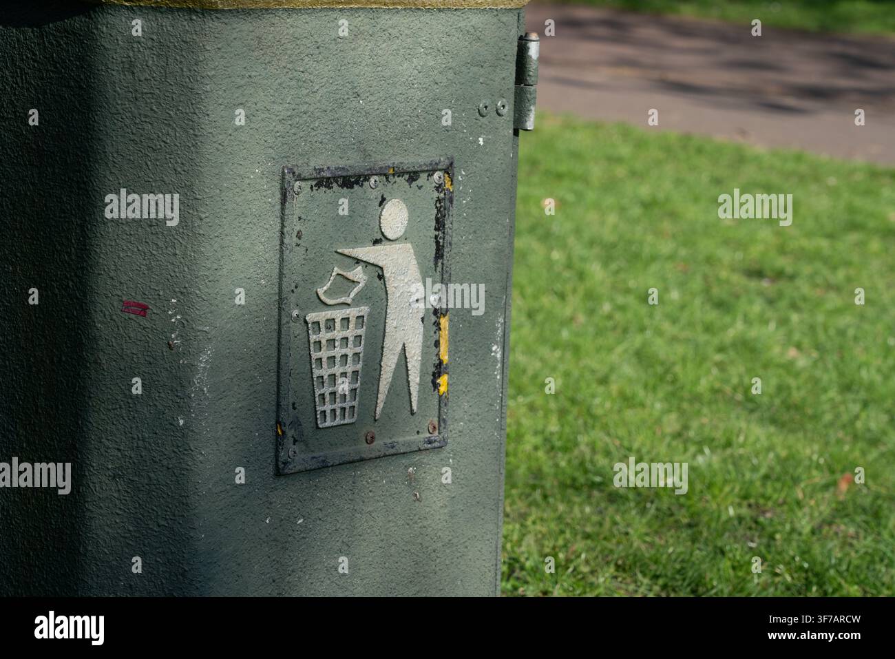 Une poubelle de parc public arborant une icône de mise à la poubelle, incitant les visiteurs à garder les lieux propres en jetant correctement leurs déchets. Banque D'Images