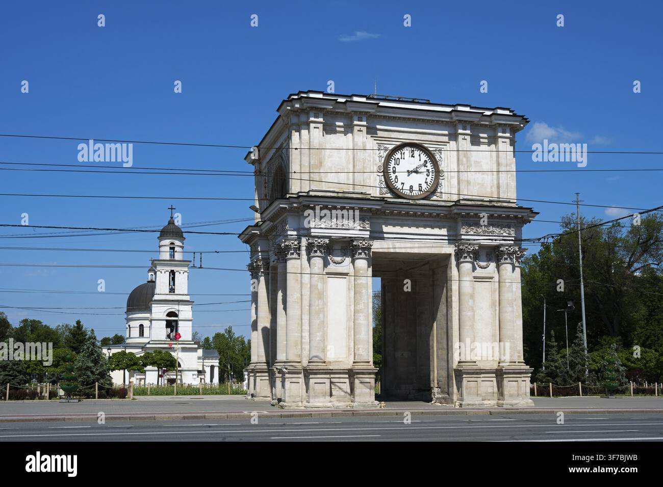 Arc de triomphe avec horloge au premier plan, église en arrière-plan sous un ciel bleu par une journée ensoleillée, Arc de triomphe et Cathédrale de la Nasterea D Banque D'Images