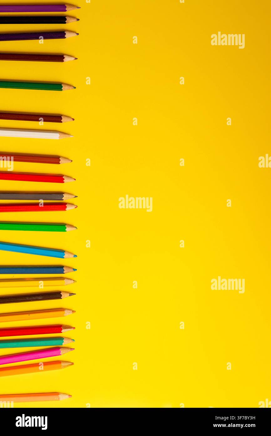Une rangée de crayons de couleur est posée sur un fond jaune. Les crayons sont alignés soigneusement, montrant diverses couleurs pour les fournitures scolaires. Cette scène se pr Banque D'Images
