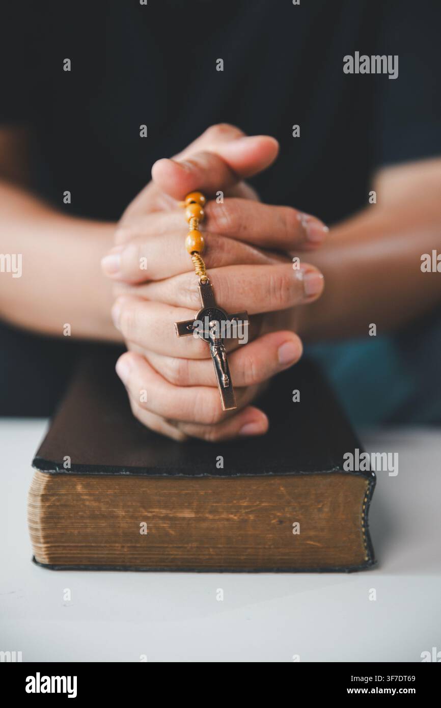 Close-up de mains jointes tenant des chapelets et un crucifix au-dessus d'une vieille Bible Sainte, représentant la prière catholique, la foi chrétienne, la dévotion, l'espoir, Banque D'Images
