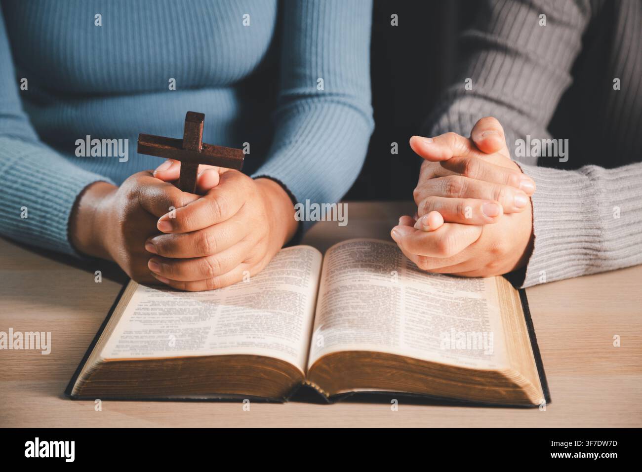 Mains tenant une croix en bois dans la prière au-dessus d'une Bible ouverte, montrant la foi chrétienne, l'adoration, le salut, la grâce, la dévotion spirituelle et l'espoir en des temps difficiles Banque D'Images