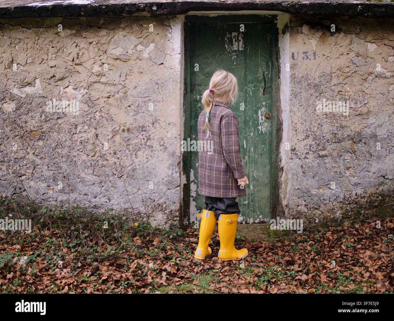 Enfant en bottes de pluie jaunes à côté d'une porte verte Banque D'Images