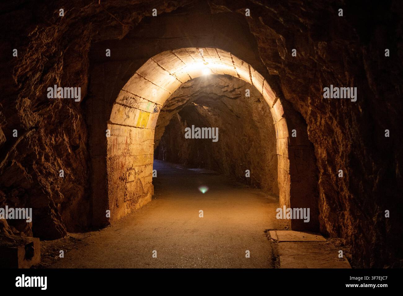 Un arc ancien magnifiquement illuminé se dresse dans un tunnel sombre, créant une atmosphère mystérieuse et historique. La vue frontale met en valeur la pierre s Banque D'Images