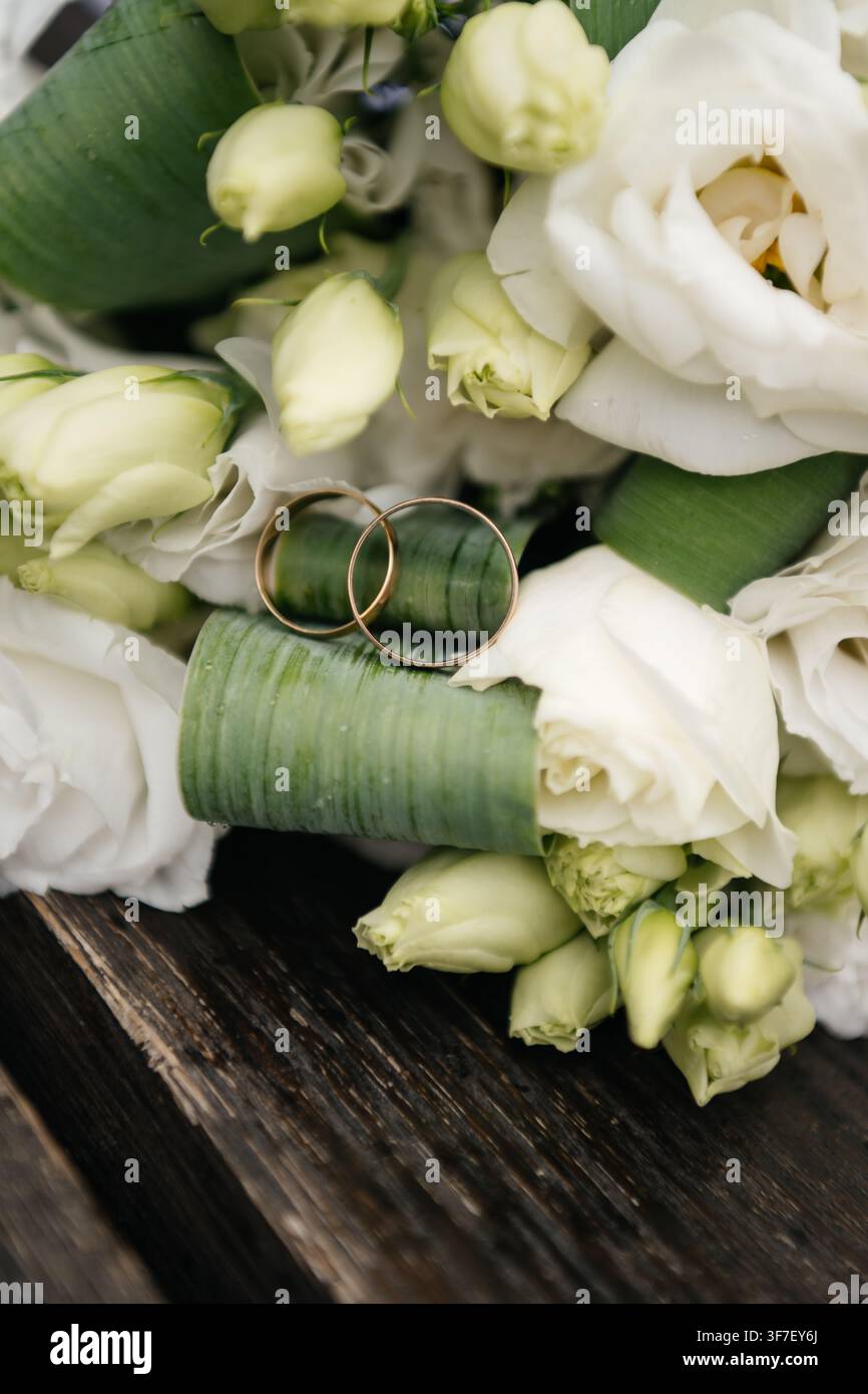 Deux alliances dorées reposant sur les tiges vertes d’un bouquet de mariée blanc Banque D'Images