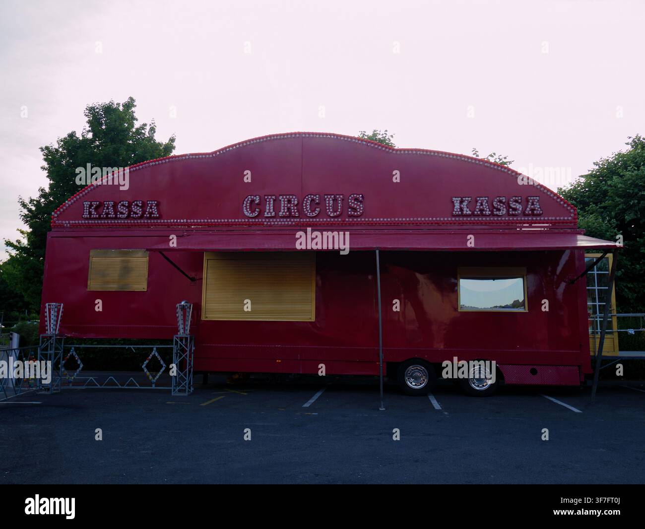 Wagon remorque de cirque rouge garé sur un terrain vide entouré d'arbres, caravane traditionnelle de cirque itinérant, véhicule de style vintage Banque D'Images