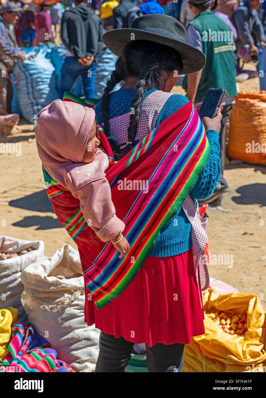 Femme indigène bolivienne en tenue traditionnelle avec un enfant utilisant un smartphone au marché du dimanche de Tarabuco, Bolivie. Banque D'Images