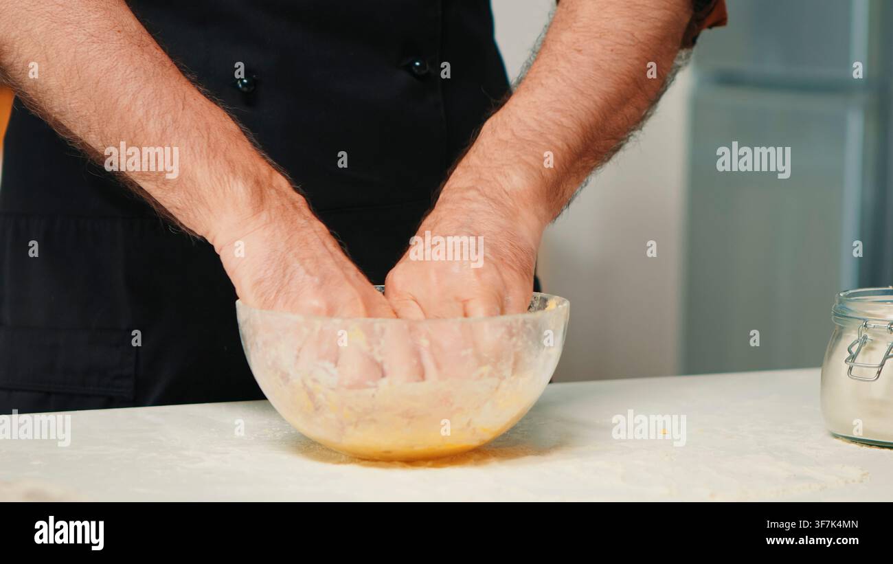 Chef à la retraite portant un tablier plie et presse une pâte maison dans le cadre de la préparation pratique des aliments, dans une zone de préparation de recettes domestique pendant la préparation de la pâte. Banque D'Images