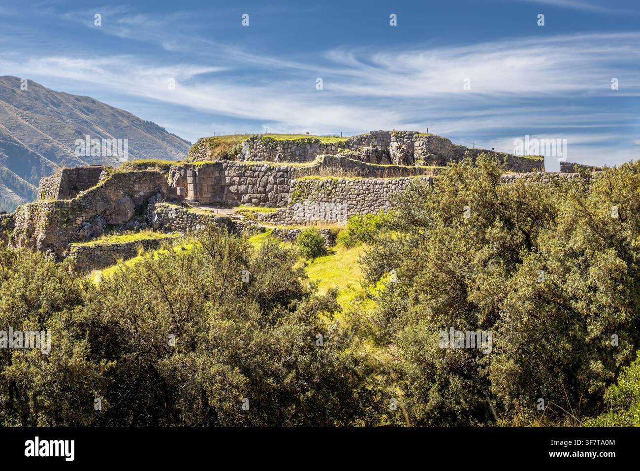 Ancienne forteresse inca de Puka Pukara s'élevant au-dessus des murs de pierre en terrasses et de la végétation luxuriante des Andes avec un paysage montagneux au loin sous un ciel bleu clair Banque D'Images