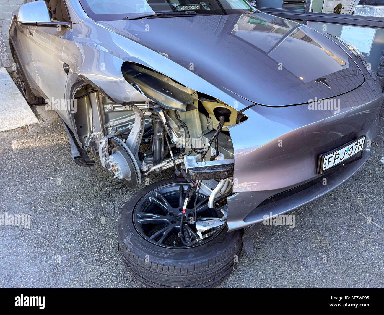 Dommages corporels sur une Tesla Model Y suite à un accident de voiture, travaux de réparation de garage sur l'aile avant - Image de stock capturée avec un smartphone