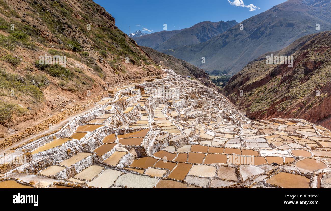 Étangs salants en terrasses traditionnels de Salineras de Maras dévalant le flanc des Andes avec des couleurs minérales vibrantes et un paysage de vallée dramatique Banque D'Images