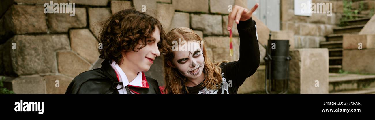 En-tête de adolescents en costumes d'Halloween célébrant et tenant un ver de bonbons Banque D'Images