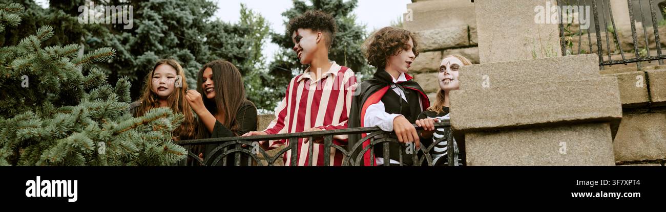 En-tête d'enfants divers en costumes d'Halloween debout près d'une rambarde en pierre Banque D'Images
