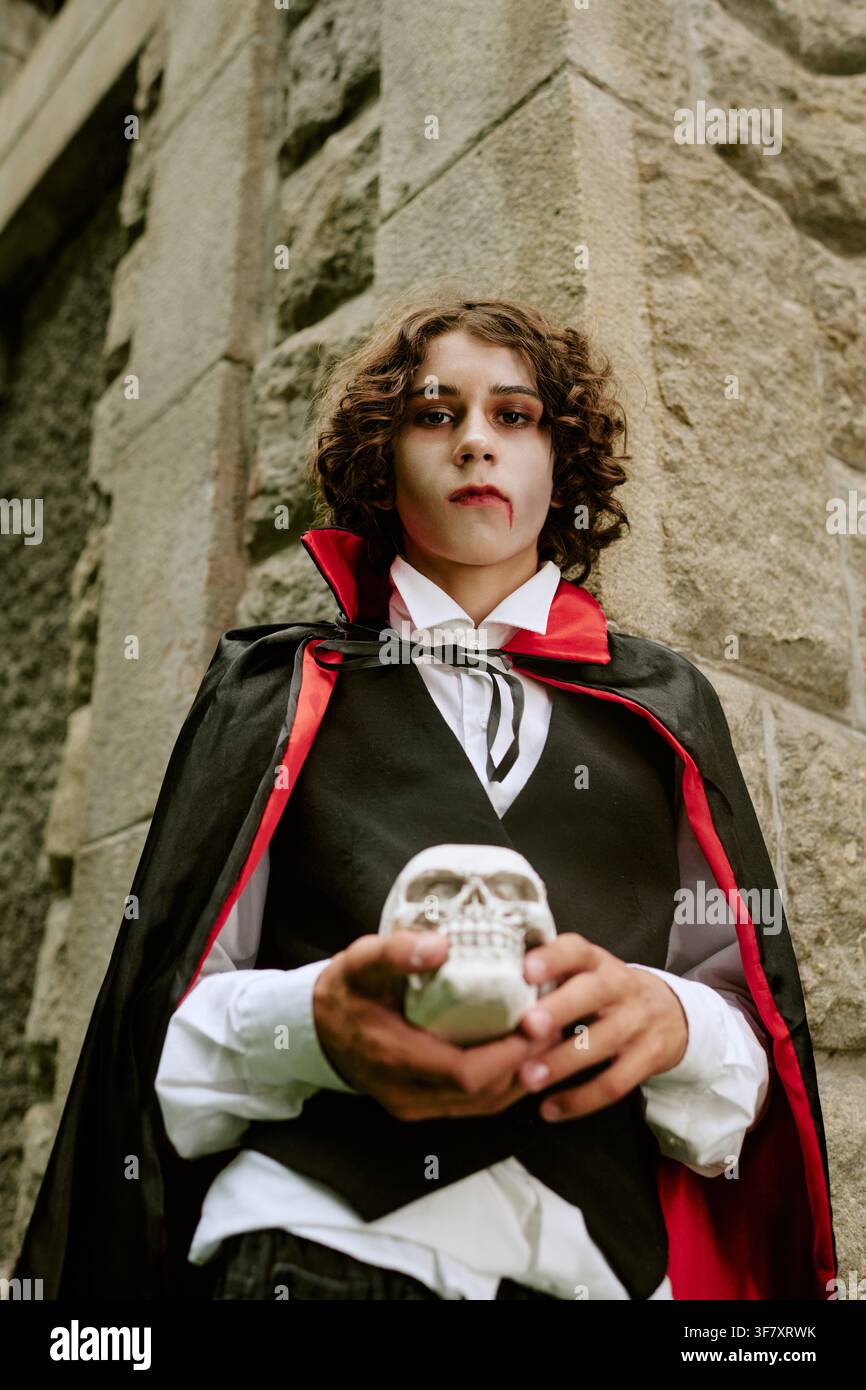 Portrait d'un adolescent en costume de vampire tenant un crâne pour Halloween Banque D'Images