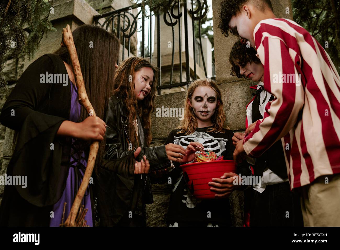 Enfants divers en costumes d'Halloween rassemblés autour d'un seau à bonbons Banque D'Images
