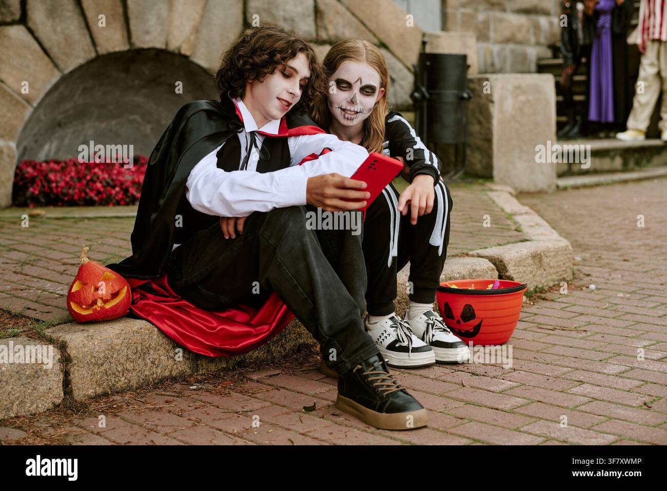 Adolescents en costumes d'Halloween utilisant un smartphone en plein air Banque D'Images