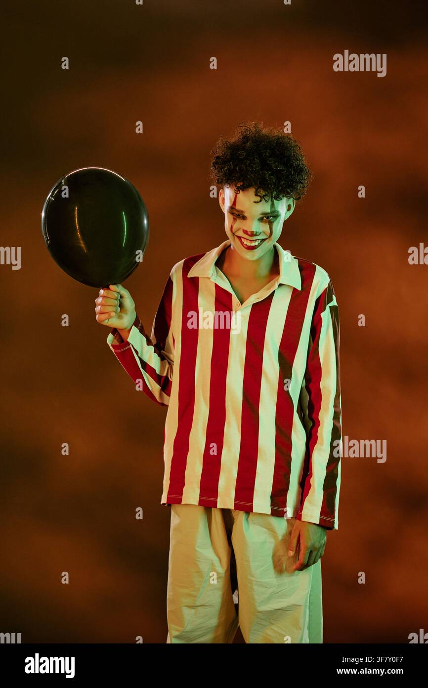 Portrait d'un adolescent en maquillage de clown tenant un ballon pour Halloween Banque D'Images