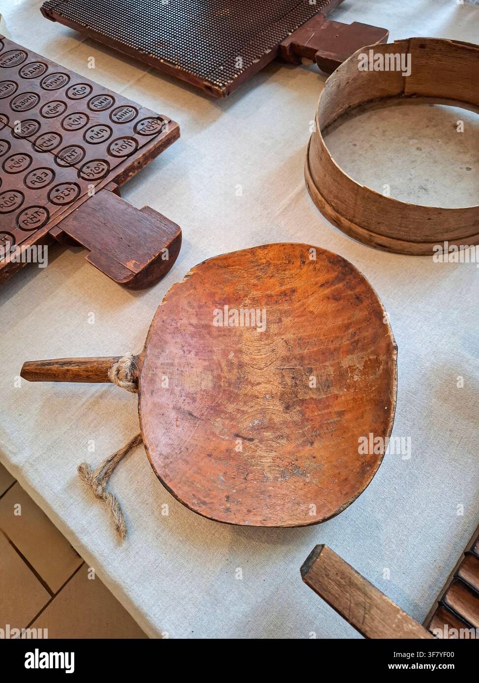 Une cuillère à pain en bois et un tamis à farine reposent sur une nappe en lin naturel parmi d'autres outils de cuisine anciens. Cette scène met en valeur le charme de la tradition Banque D'Images